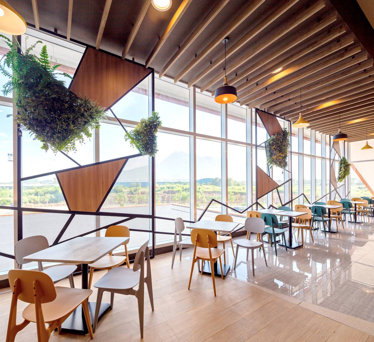 The dining area at SM City Sto. Tomas features floor-to-ceiling windows that offer views of Mt. Makiling, seamlessly connecting the indoor space with nature. Geometric panels, suspended greenery, and warm finishes create a modern yet inviting atmosphere, enhancing the overall customer experience.
