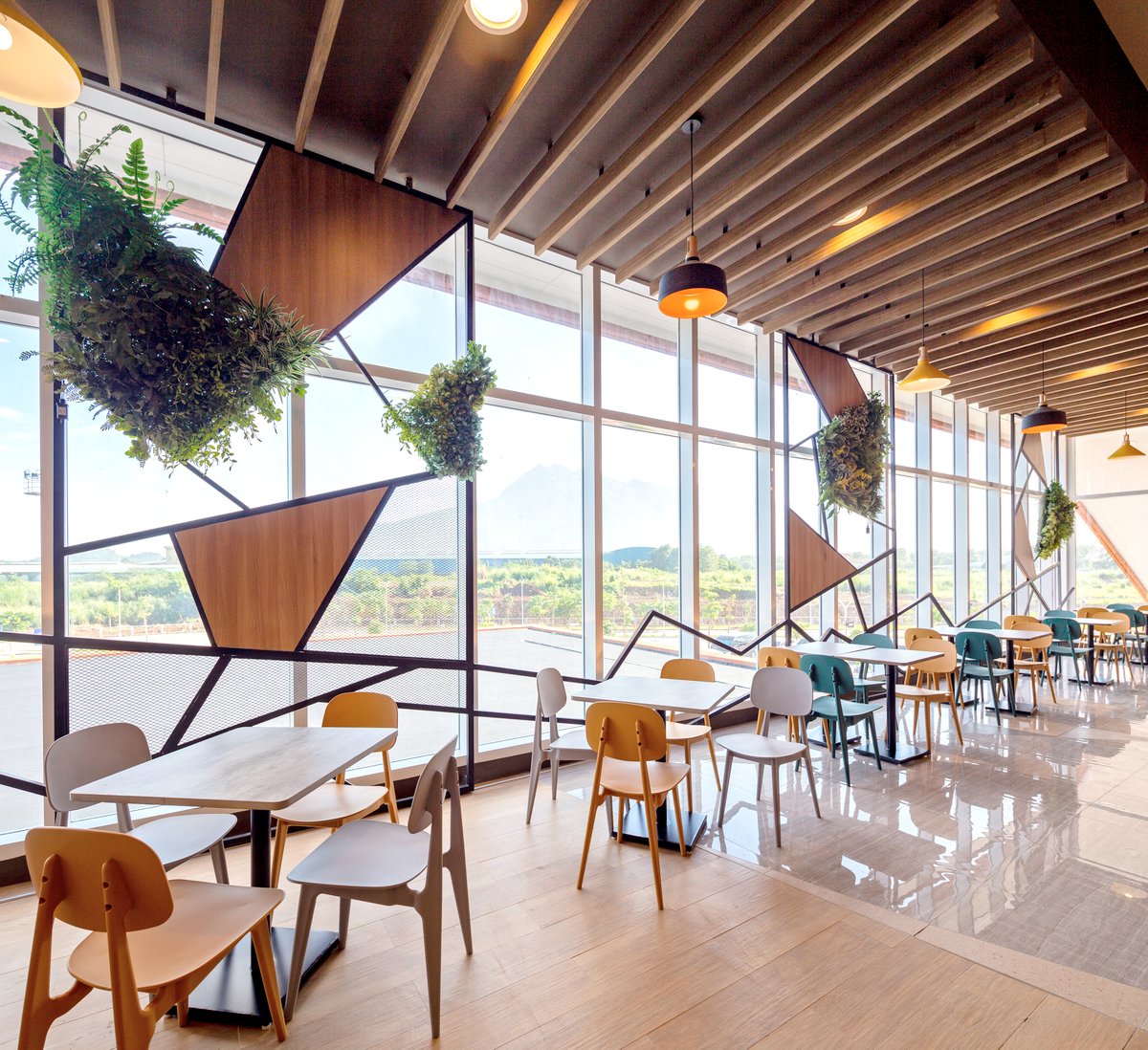 The dining area at SM City Sto. Tomas features floor-to-ceiling windows that offer views of Mt. Makiling, seamlessly connecting the indoor space with nature. Geometric panels, suspended greenery, and warm finishes create a modern yet inviting atmosphere, enhancing the overall customer experience.