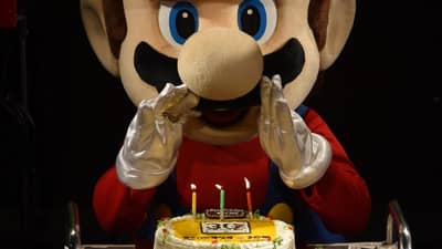 (FILES) This file photo taken on September 13, 2015 shows "Super Mario" attempting to blow out the candles on a cake during celebrations and a live performance of the most well-known Mario music to mark the game's 30th anniversary in Tokyo. Over four decades Nintendo's mascot "Super Mario" has run and jumped his way to global stardom, broadening the appeal of the video game industry as one of its top characters. September 13, 2025 will mark the 40th anniversary of the release of the 'Super Mario Bros' video game by Japanese video game maker Nintendo.