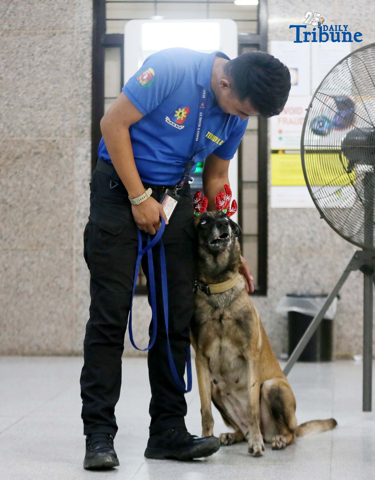 A K9 handler holds his trained partner, a K9 dog dressed in Christmas accessories, while on duty at the Office of the Ombudsman in Quezon City.