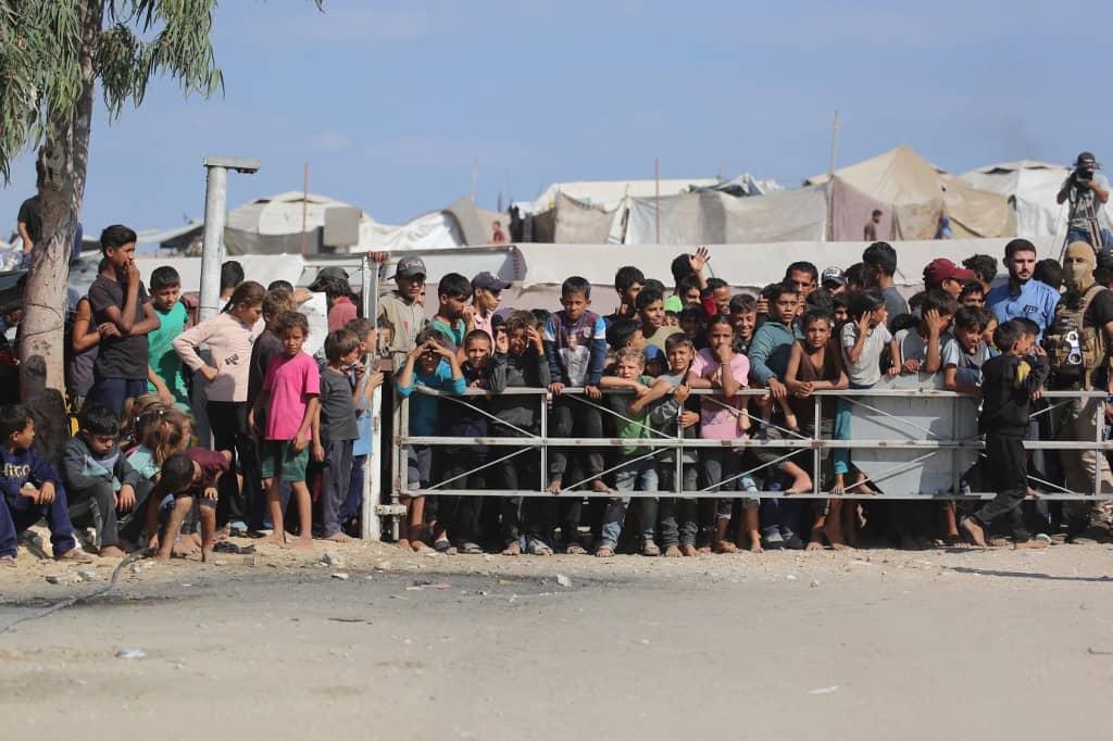 A Palestinian militant (R) fighter of the Ezzedine al-Qassam Brigades, the military wing of Hamas, stands guard next to a crowd watching the transfer of released Israeli hostages to the Red Cross in the south of Deir el-Balah in the central Gaza Strip, on 13 October 2025. The Palestinian militant group has handed over to the Red Cross a second group of 13 Israeli hostages released on 13 October.

Bashar TALEB / AFP