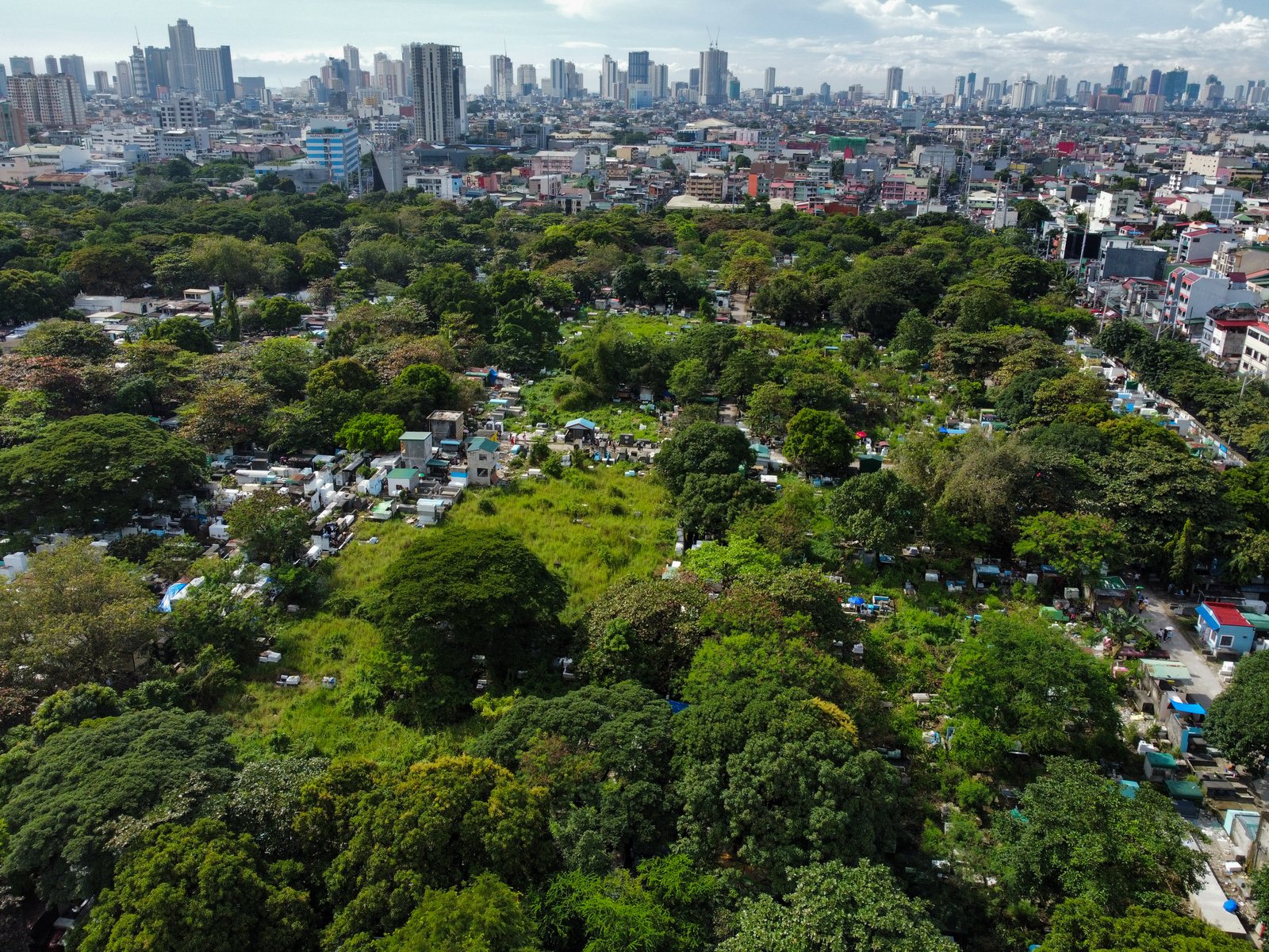 The vast greenery of Manila South Cemetery stands in contrast with the modern tall buildings of Makati City in this photo taken on All Saints' Day. As of 1:00 in the afternoon, at least 46,000 people have visited the Manila South Cemetery.