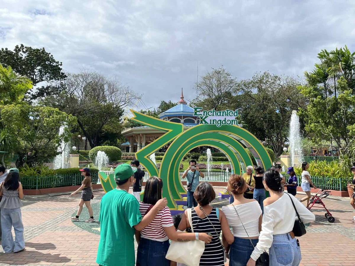 People fall in line to take photos with the giant 30 sign at the entrance of Enchanted Kingdom.