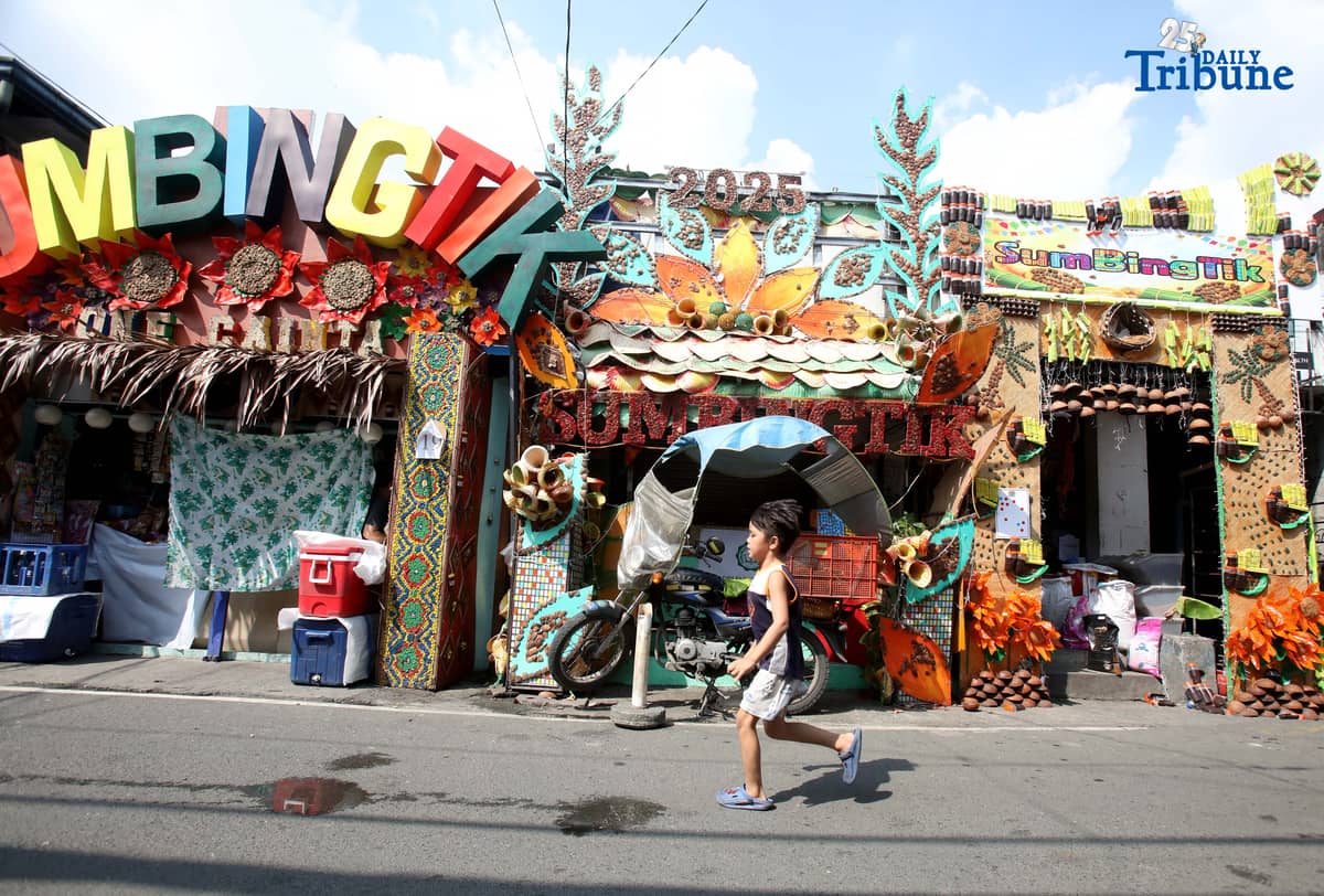 (December 01 2025) Pedestrians walk past houses decorated with colourful reusable materials as part of the 2025 SumBingTik (Suman, Bibingka, Latik) Festival in Cainta, Rizal on Monday December 1 2025. The SumBingTik Festival is an annual cultural long-week festival held in Cainta, Rizal, along with the town's founding anniversary and the feast of Our Lady of Light which is celebrated on December 1, the patron saint of the town. The festival was first celebrated in 2014. Photo/Analy Labor