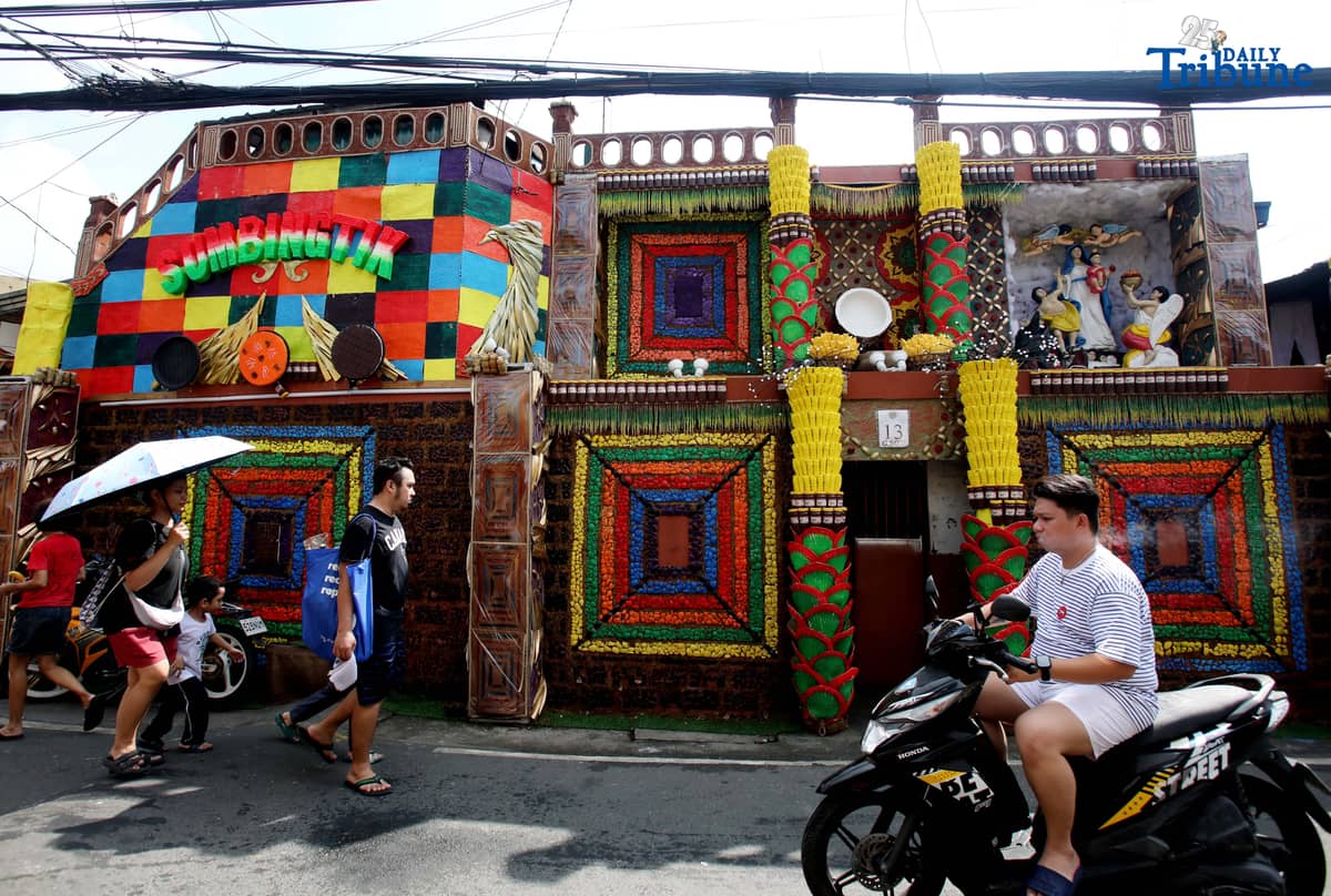 (December 01 2025) Pedestrians walk past houses decorated with colourful reusable materials as part of the 2025 SumBingTik (Suman, Bibingka, Latik) Festival in Cainta, Rizal on Monday December 1 2025. The SumBingTik Festival is an annual cultural long-week festival held in Cainta, Rizal, along with the town's founding anniversary and the feast of Our Lady of Light which is celebrated on December 1, the patron saint of the town. The festival was first celebrated in 2014. Photo/Analy Labor