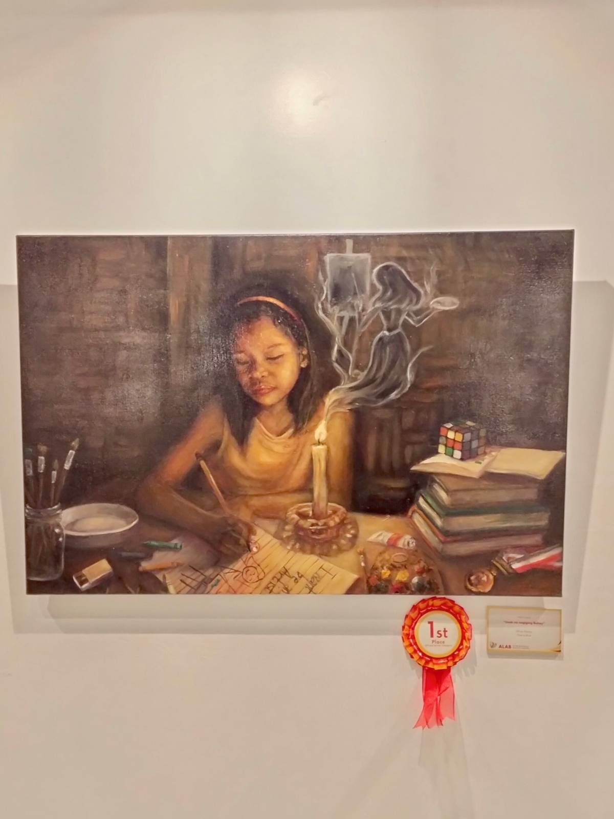 "Usok na nagiging Buhay" by Ruth Cenas, first place winner in the Oil/Acrylic category, depicts a young girl drawing under the glow of a single candle. Even without electricity, the candle’s light and the fire within her allow her to dream of becoming an artist and continue pursuing her craft.