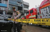A member of the Indonesian police sets up a barricade tape to cordon off a seven-storey building where firefighters extinguished a fire that killed at least 20 people in central Jakarta on December 9, 2025.