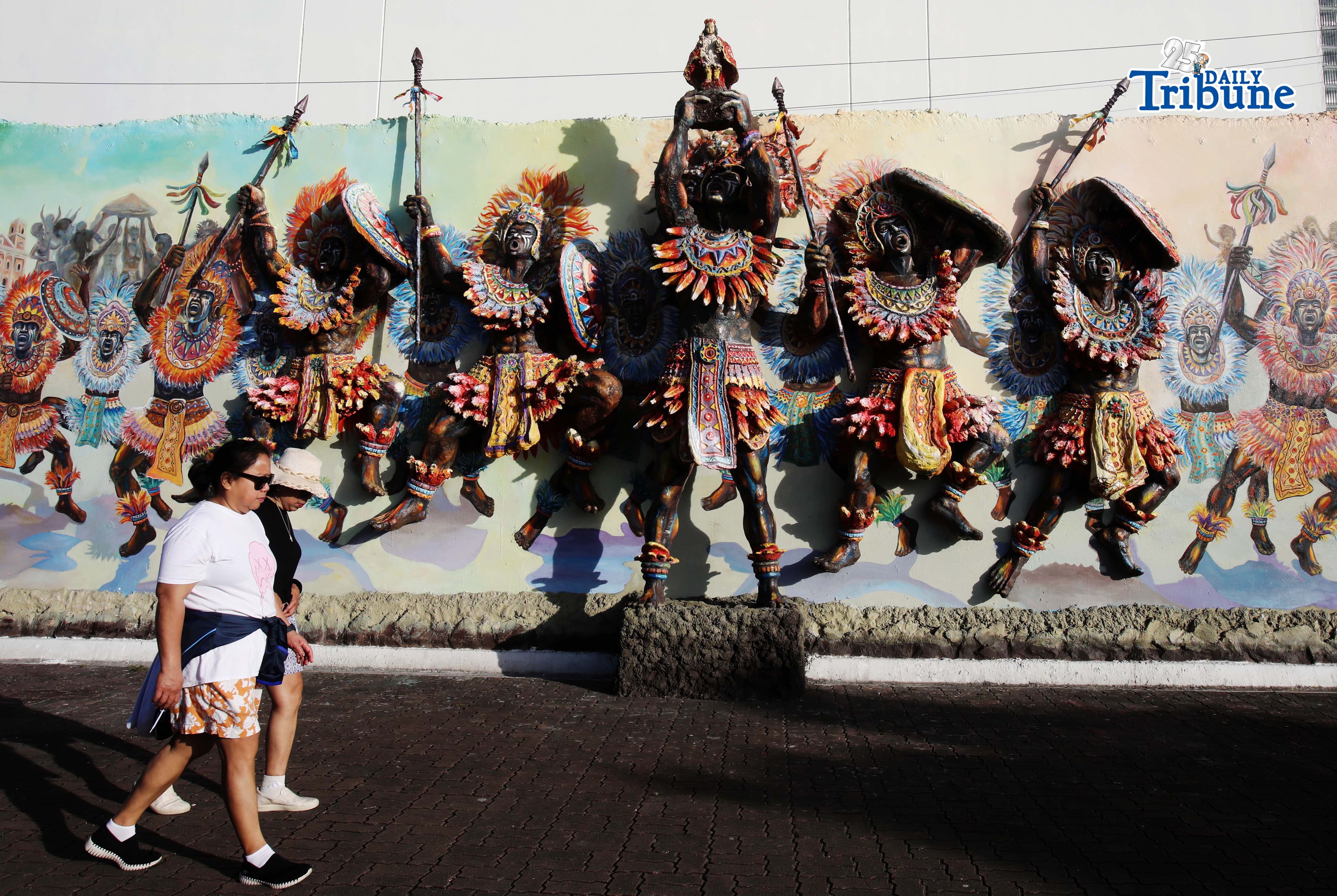 Local tourists walk past the Dinagyang warriors mural at the Iloilo river Esplanade on Saturday January 24 2026. The 3D mural vividly showcases Dinagyang warriors leaping victoriously, symbolizing the spirited nature of the Ilonggos. These warriors, depicted with intense devotion, leap with pride and bravery, echoing celebrations and honor for Senior Santo Niño, creating a dynamic and celebratory scene. Photo/Analy Labor