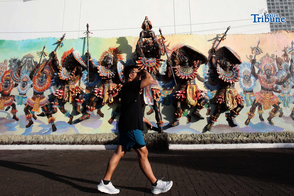 (January 24 2026) Local tourists walk past the Dinagyang warriors mural at the Iloilo river Esplanade on Saturday January 24 2026. The 3D mural vividly showcases Dinagyang warriors leaping victoriously, symbolizing the spirited nature of the Ilonggos. These warriors, depicted with intense devotion, leap with pride and bravery, echoing celebrations and honor for Senior Santo Niño, creating a dynamic and celebratory scene. Photo/Analy Labor