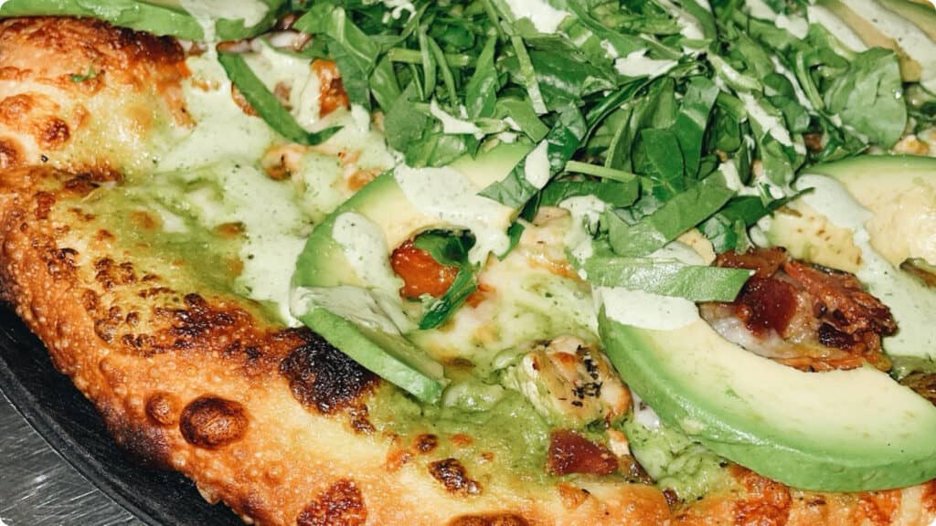 THE California Sunrise pizza — featuring green goddess dressing, roasted chicken, and peppered bacon, all topped with fresh avocado and chiffonade spinach — is one of the bestsellers.