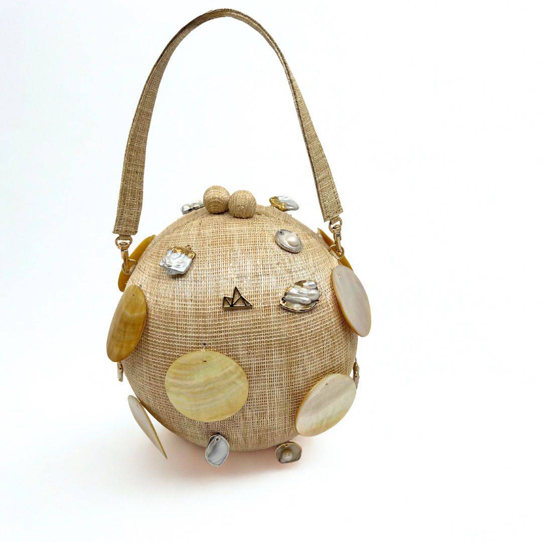 VESTI'S Taklobo Ball Bag is thoughtfully designed and inspired by the graceful curves of the taklobo in Filipino, meaning ‘giant clam.’ Crafted with the natural beauty of our Philippine abaca fabric and accented with shimmering capiz, baroque mother-of-pearls and gold-tone rings, the Vesti Taklobo ball bag represents courage with sculptural statement in Filipino craft. It fits an iPhone Pro Max and other essentials. Can stand alone. Exclusive and in limited edition.