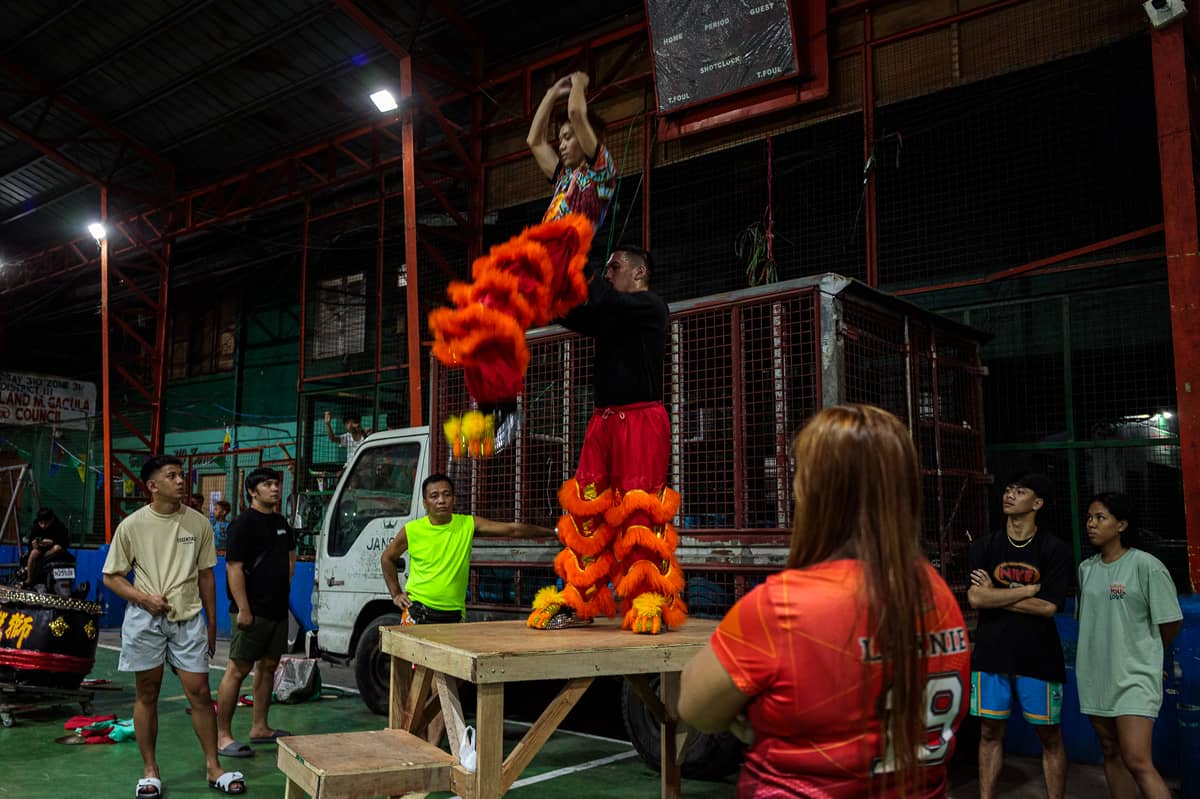 Members of the Philippine Rui Dragon Dance group look on as Jhayvee Sicat ang King Noah rehearse their lion dance routine at a basketball court in downtown Manila on Friday, 6 February 2026.