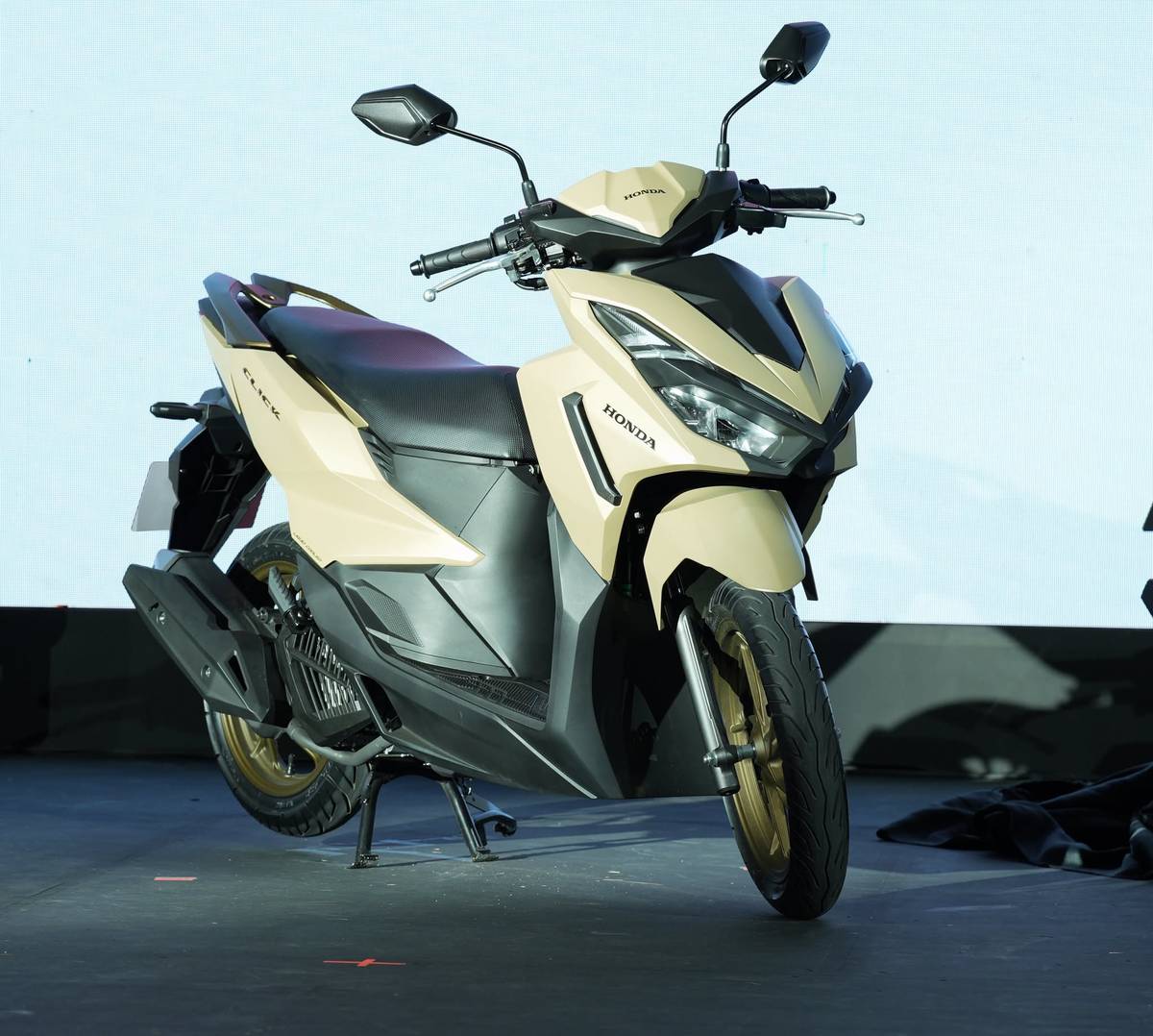 BEIGE variant of the Honda Click125 stands on display, showing its updated body lines and gold wheel accents.
