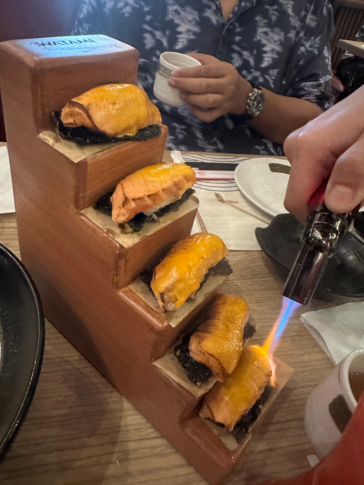 THIS ladder of Salmon Aburi Tacos gets torched right at the table, adding a fun show element to your meal.