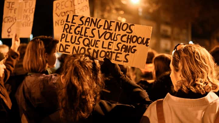protestor holds a sign reading "The blood of our period shock you more than the blood of our dead" as people take part in a torchlight procession organised by "Nous Toutes" (All of Us), a French feminist collective, against sexist and violence to women, in Rennes, western France, on November 25, 2022, during the International Day for the Elimination of Violence Against Women.