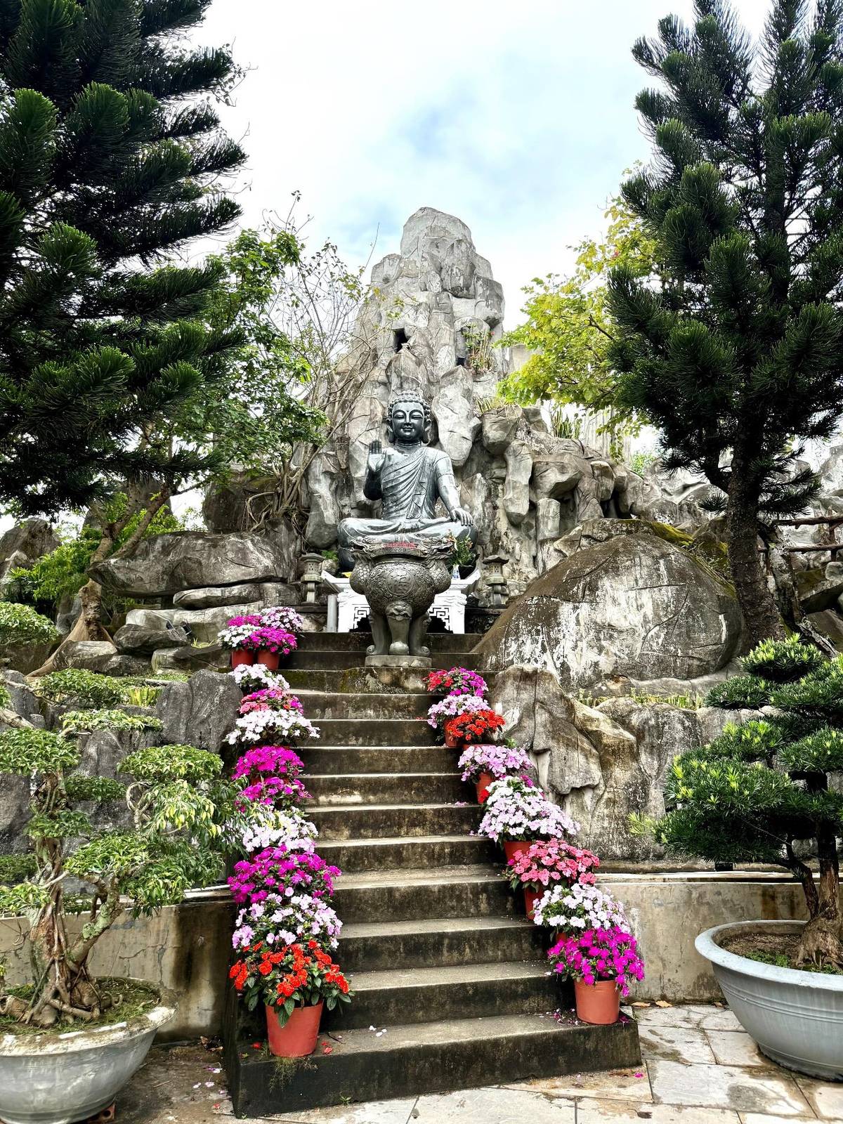 POTS full of blooms honor the sitting Buddha.