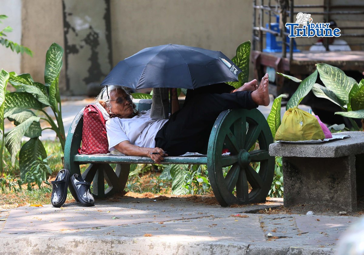(April 22 2026) A woman lying at the bench in Quezon City Circle, covering an umbrella to protect herself from the heat while answering the newspaper crossword puzzle on wednesday April 22 2026. Photo/Analy Labor