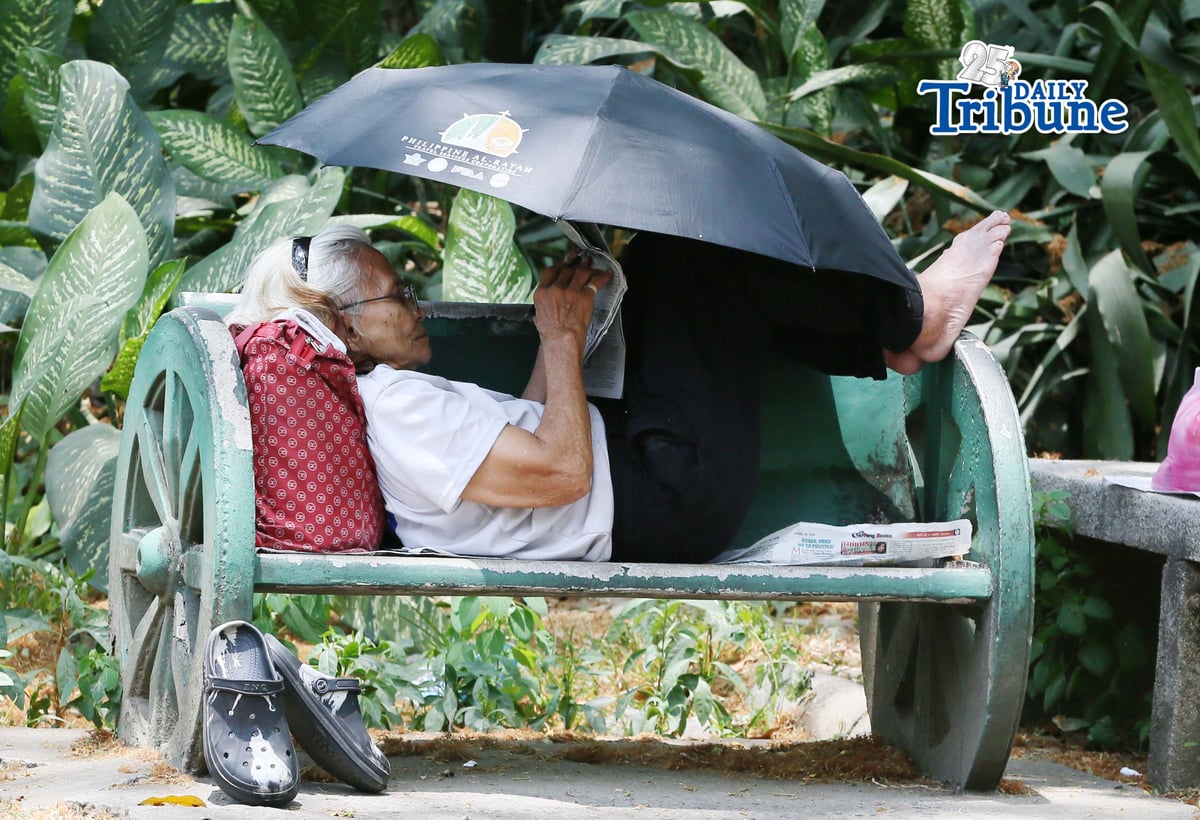 (April 22 2026) A woman lying at the bench in Quezon City Circle, covering an umbrella to protect herself from the heat while answering the newspaper crossword puzzle on wednesday April 22 2026. Photo/Analy Labor