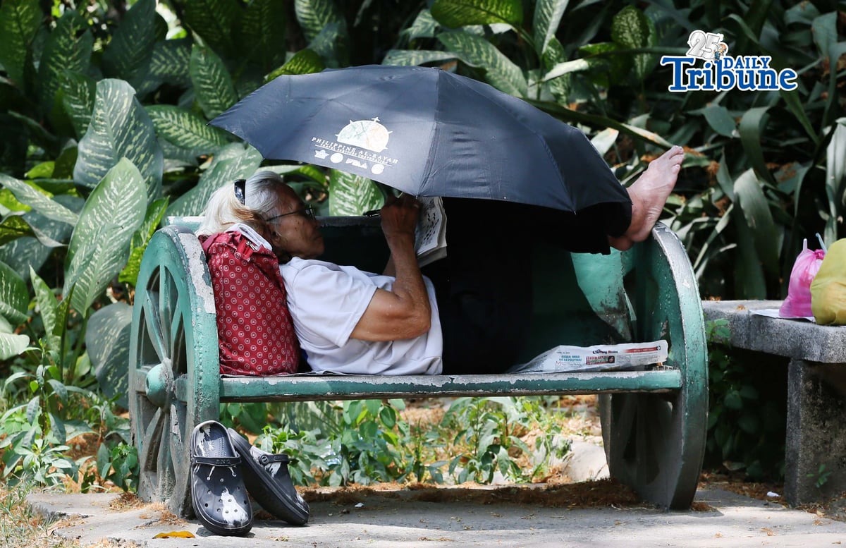 (April 22 2026) A woman lying at the bench in Quezon City Circle, covering an umbrella to protect herself from the heat while answering the newspaper crossword puzzle on wednesday April 22 2026. Photo/Analy Labor