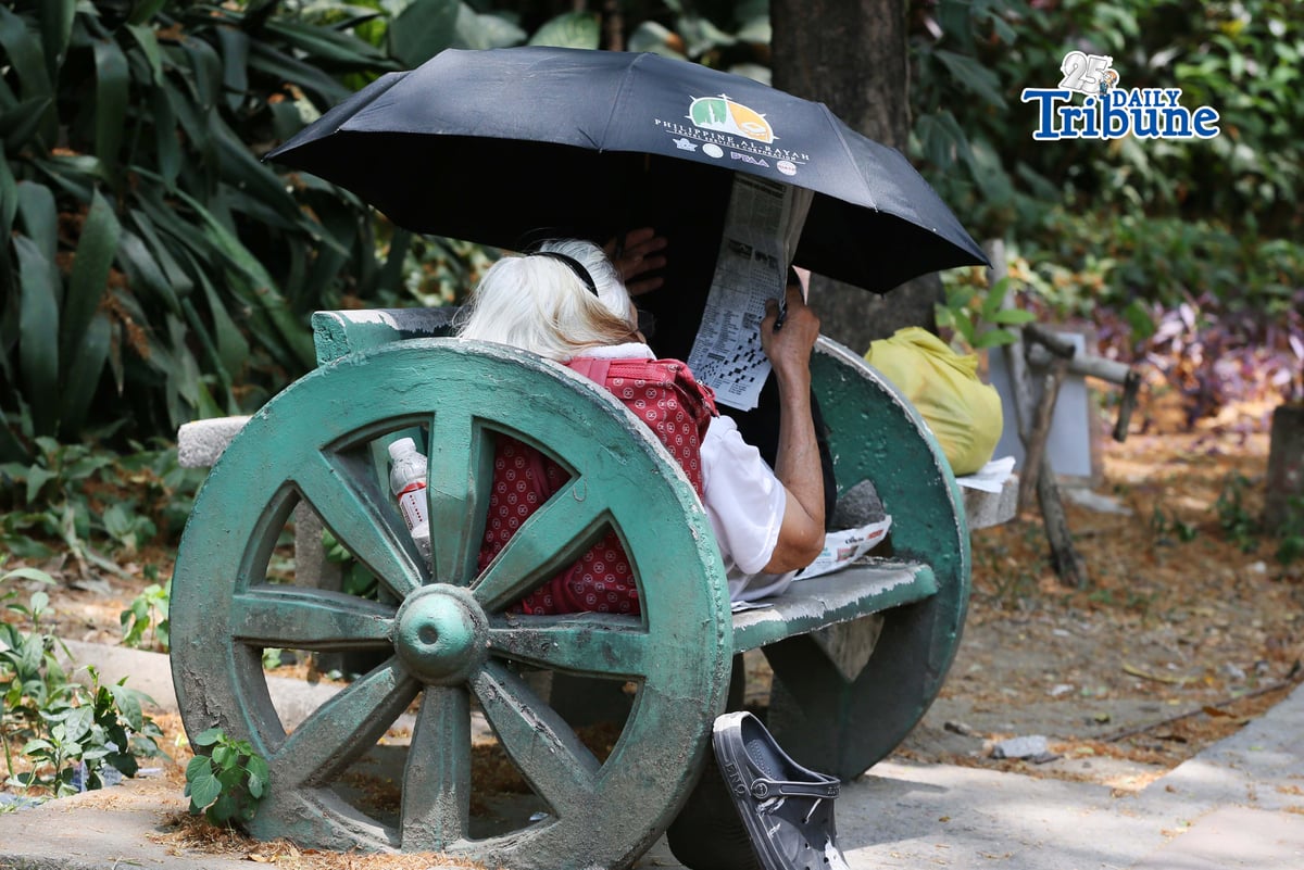 (April 22 2026) A woman lying at the bench in Quezon City Circle, covering an umbrella to protect herself from the heat while answering the newspaper crossword puzzle on wednesday April 22 2026. Photo/Analy Labor