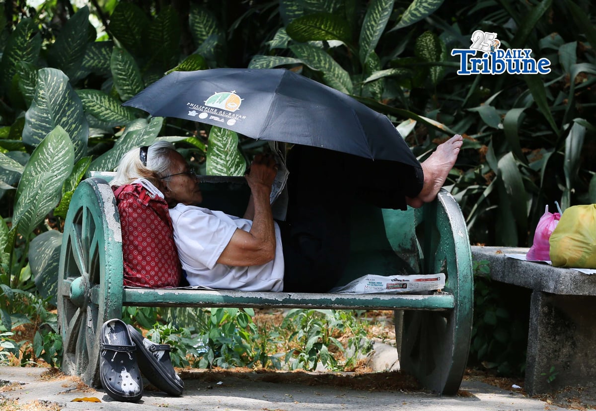 (April 22 2026) A woman lying at the bench in Quezon City Circle, covering an umbrella to protect herself from the heat while answering the newspaper crossword puzzle on wednesday April 22 2026. Photo/Analy Labor