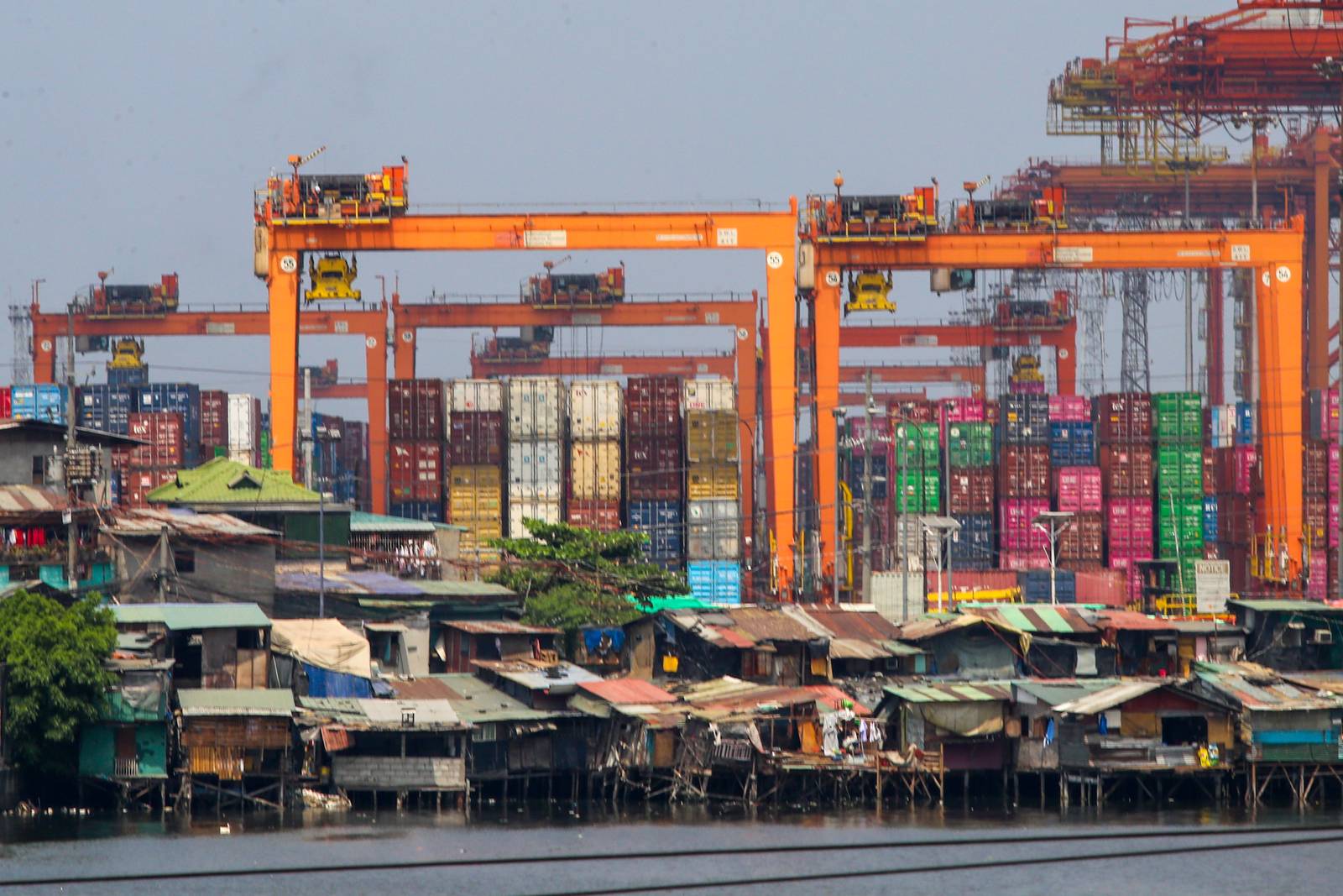 Informal settlements line the edge of the container port area in Manila, as seen from a pedestrian overpass along Mel Lopez Boulevard. A recent study by the government think tank Philippine Institute for Development Studies warns that the current oil crisis could push over 1.3 million more Filipinos into poverty as rising fuel costs lead to an immediate spike in the cost of rice, fish, meat, and vegetables.