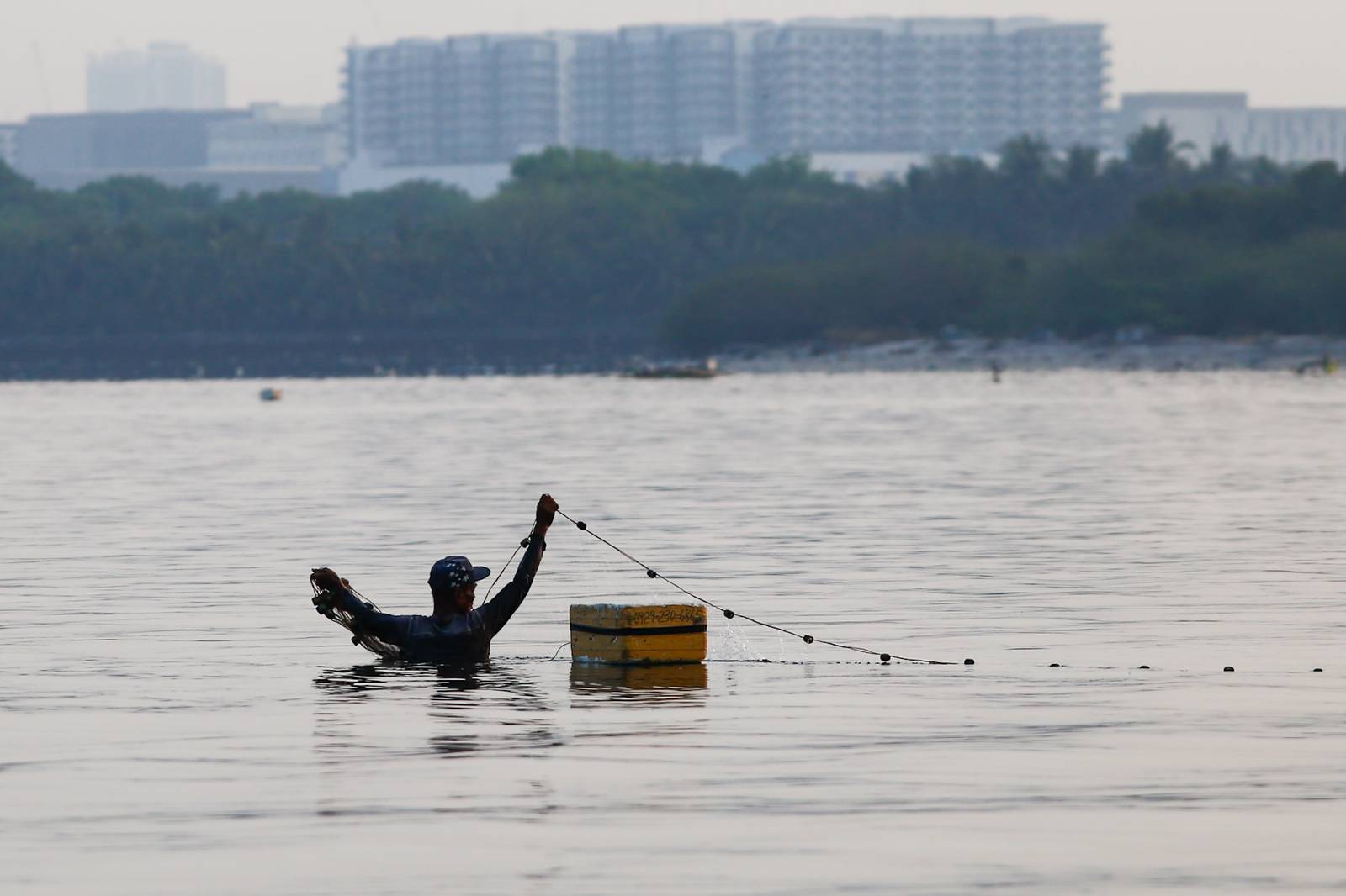 A fisherman casts his nets at a chest-deep beach in Parañaque City on Saturday. Despite the rollbacks in fuel costs, some fishermen decided not to use their motorized boats and instead use alternative methods in fishing for daily sustenance.