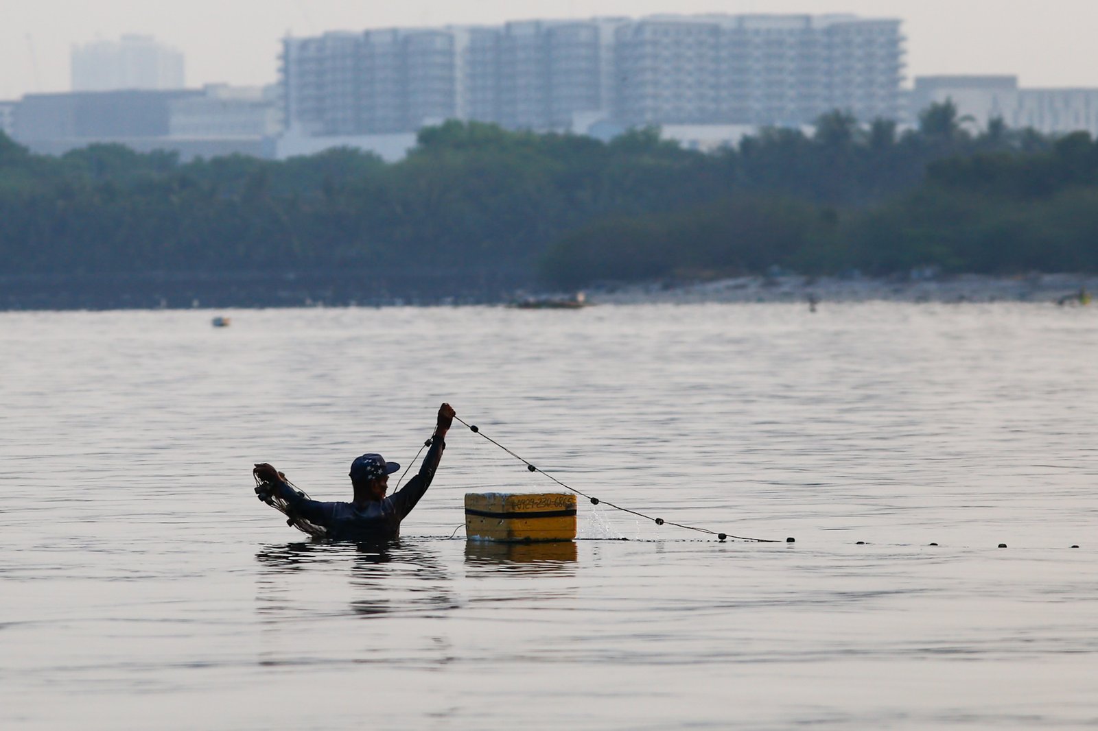 A fisherman casts his nets at a chest-deep beach in Parañaque City on Saturday. Despite the rollbacks in fuel costs, some fishermen decided not to use their motorized boats and instead use alternative methods in fishing for daily sustenance.