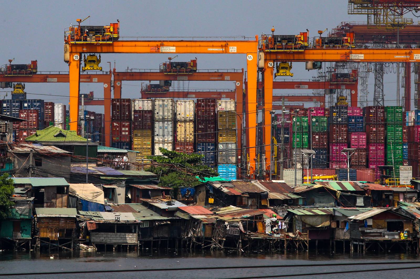Informal settlements line the edge of the container port area in Manila, as seen from a pedestrian overpass along Mel Lopez Boulevard. A recent study by the government think tank Philippine Institute for Development Studies warns that the current oil crisis could push over 1.3 million more Filipinos into poverty as rising fuel costs lead to an immediate spike in the cost of rice, fish, meat, and vegetables.