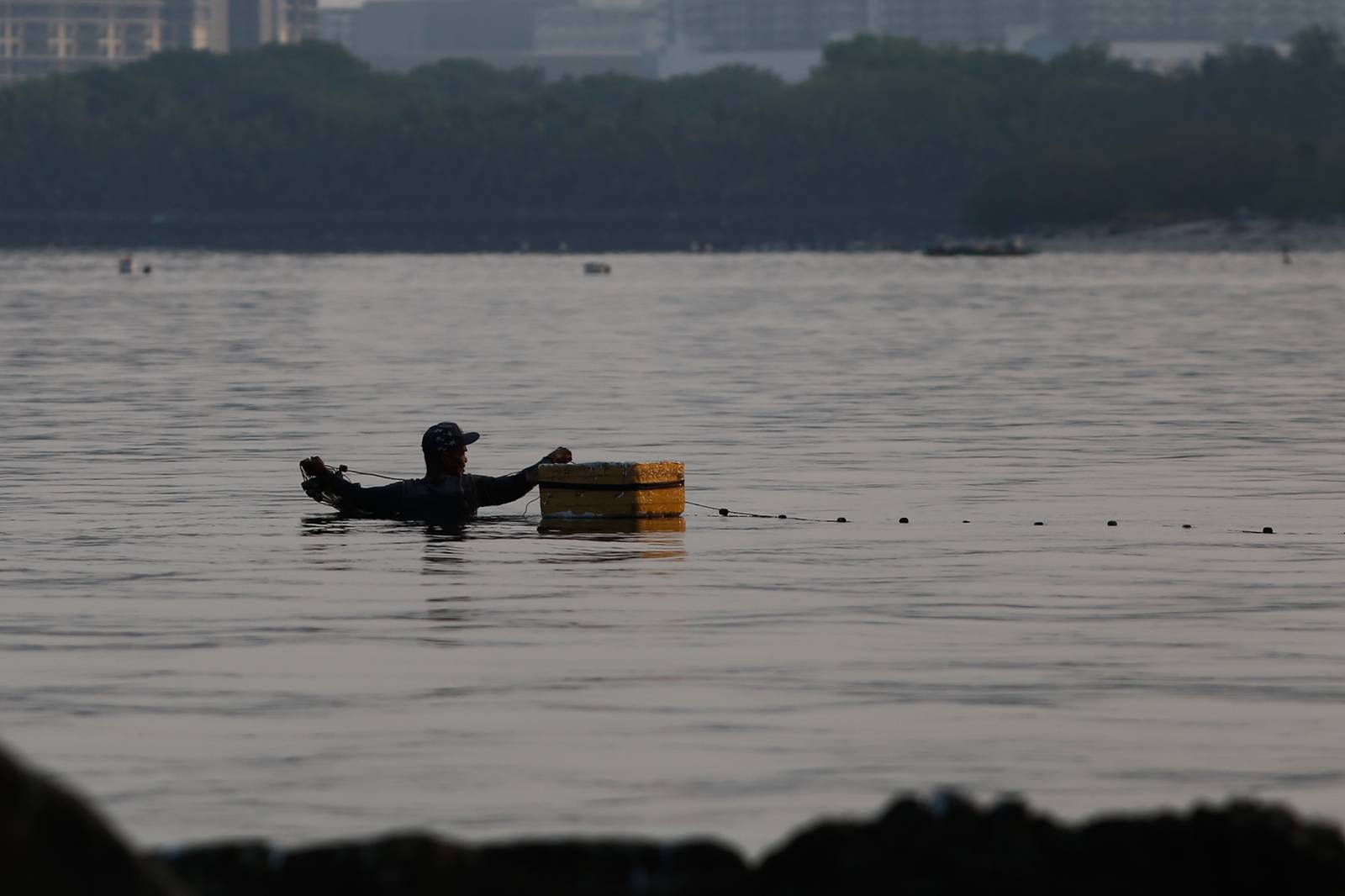 A fisherman casts his nets at a chest-deep beach in Parañaque City on Saturday. Despite the rollbacks in fuel costs, some fishermen decided not to use their motorized boats and instead use alternative methods in fishing for daily sustenance.