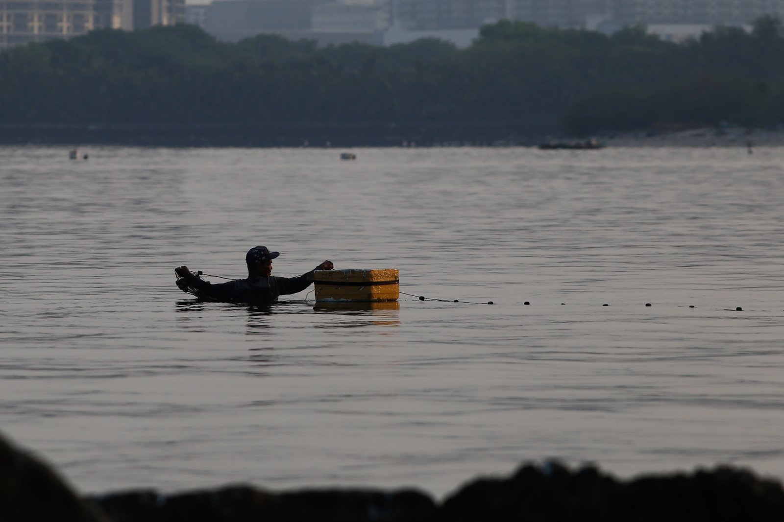 A fisherman casts his nets at a chest-deep beach in Parañaque City on Saturday. Despite the rollbacks in fuel costs, some fishermen decided not to use their motorized boats and instead use alternative methods in fishing for daily sustenance.