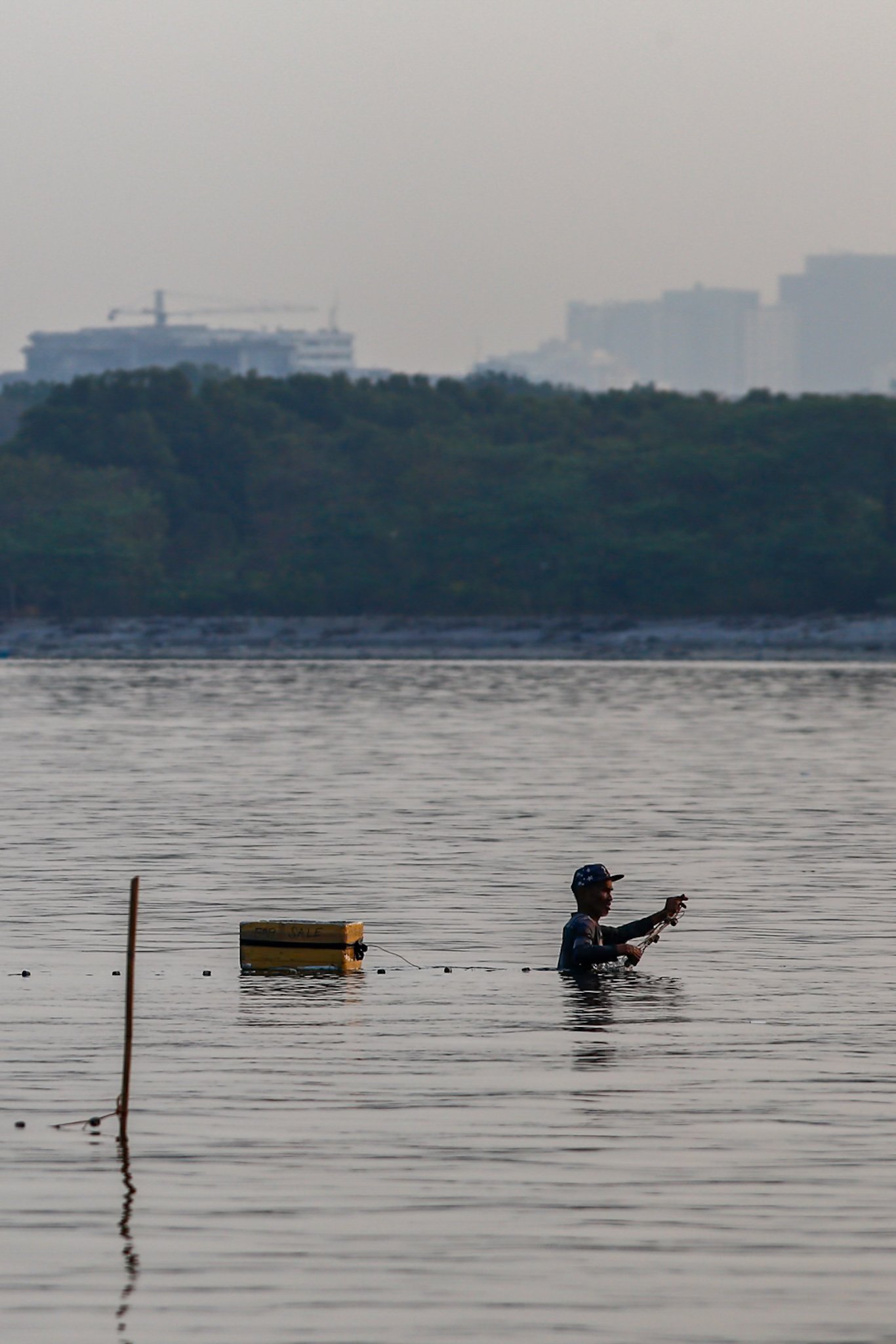 A fisherman casts his nets at a chest-deep beach in Parañaque City on Saturday. Despite the rollbacks in fuel costs, some fishermen decided not to use their motorized boats and instead use alternative methods in fishing for daily sustenance.