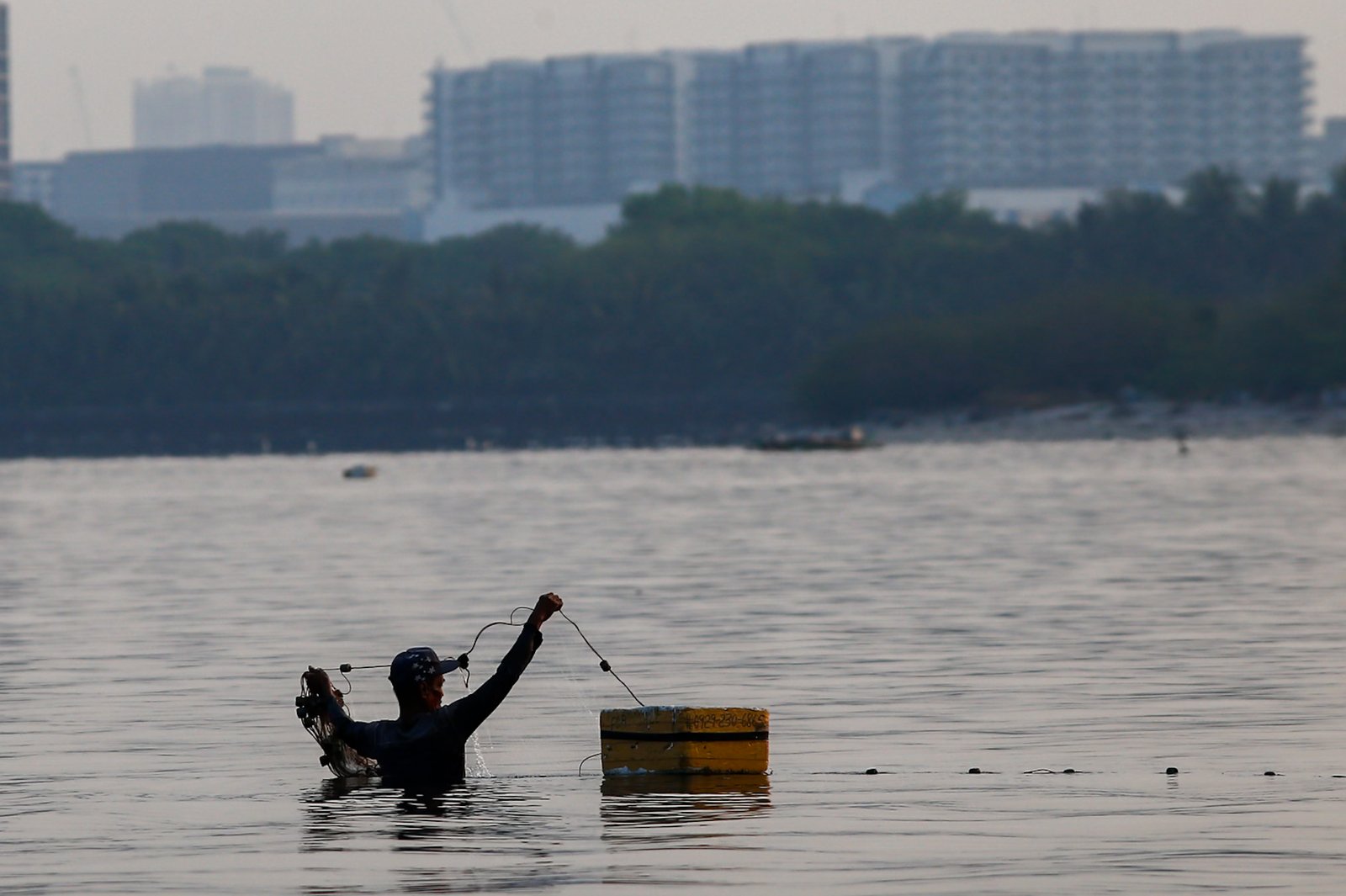 A fisherman casts his nets at a chest-deep beach in Parañaque City on Saturday. Despite the rollbacks in fuel costs, some fishermen decided not to use their motorized boats and instead use alternative methods in fishing for daily sustenance.