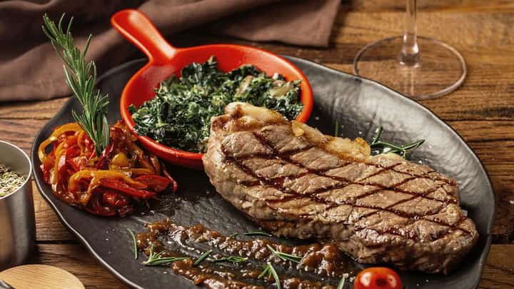 GRILLED steak with smoky, seared grill marks, juicy and tender at the center, served with a rich, flavorful sauce, sautéed vegetables and fresh garden greens.