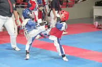 A young taekwondo jin in red armor connects with a decisive head kick during a sparring match in the previous SMART/MVPSF Summer Clinic.