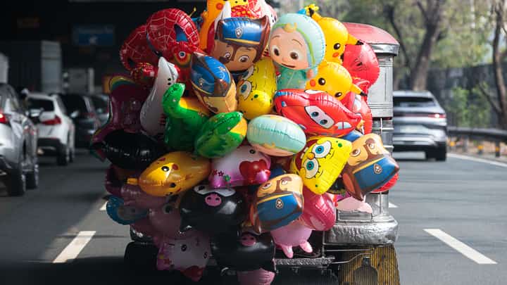 A vendor selling cartoon-shaped party balloons sits on the stepboard of a jeepney as it cruises along the South Luzon Expressway (SLEX) northbound in Makati City on Saturday, 16 May 2026.