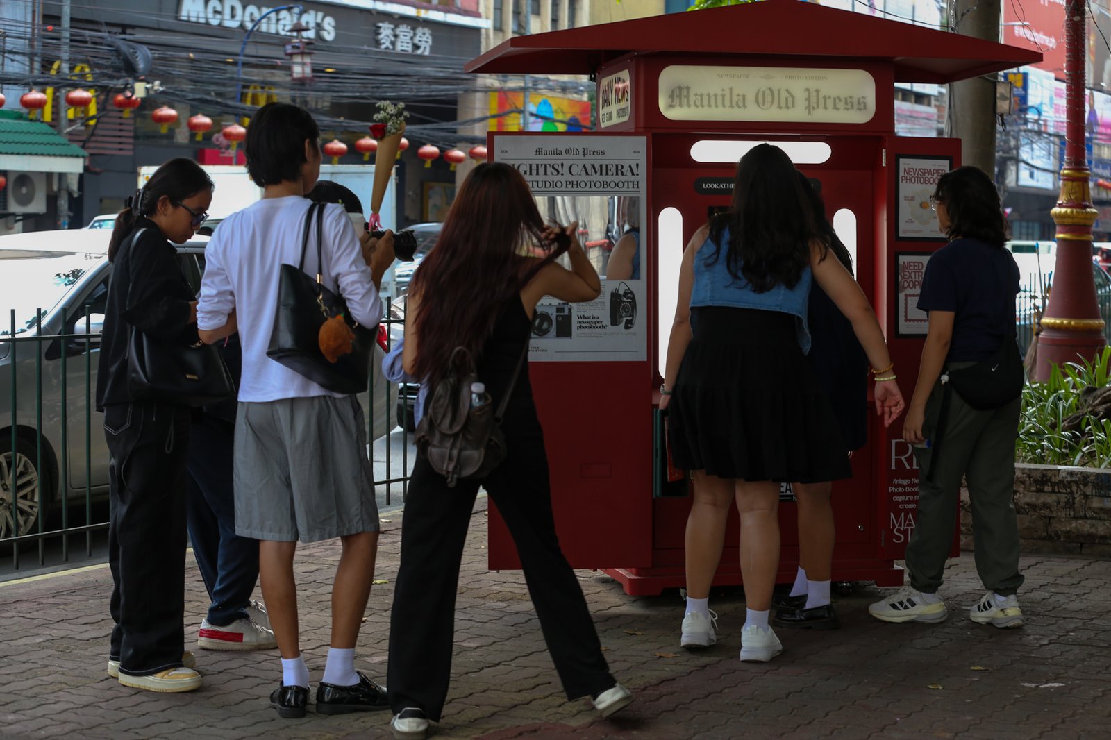 Tourists line up for a photo session at a booth in Plaza San Lorenzo Ruiz in Binondo, Manila on Saturday, 20 June 2026. The photo booth, which prints a vintage-style newspaper alongside a downloadable digital copy, is becoming a popular destination for Binondo-goers.
