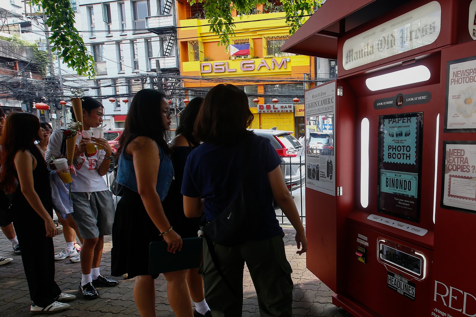 Tourists line up for a photo session at a booth in Plaza San Lorenzo Ruiz in Binondo, Manila on Saturday, 20 June 2026. The photo booth, which prints a vintage-style newspaper alongside a downloadable digital copy, is becoming a popular destination for Binondo-goers.