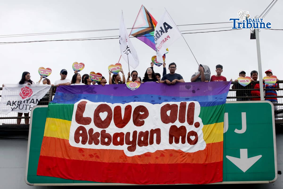 A day before the annual Pride March, volunteers from Akbayan Youth unfurl a rainbow banner reading, “Love All, Akbayan Mo! #PrideEquality,” on the Philcoa footbridge in Quezon City on Friday, calling for equality, dignity and recognition of every person's identity. | Photo by Analy Labor