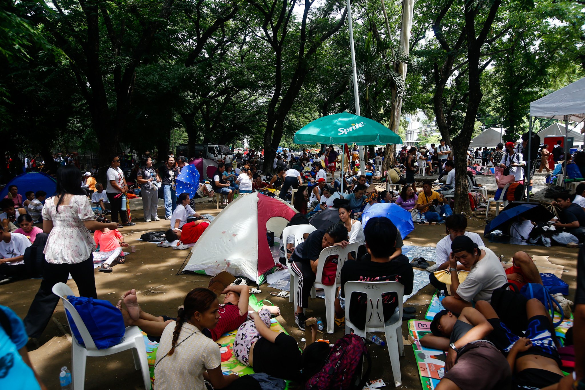 Members of Iglesia ni Cristo and their allies seek shade under trees at Liwasang Bonifacio in Manila on 02 July 2026 as they wait for the start of their protest rally. The organizers relocated the rally from the EDSA People Power Monument in Quezon City after their permit to hold the event there was revoked.