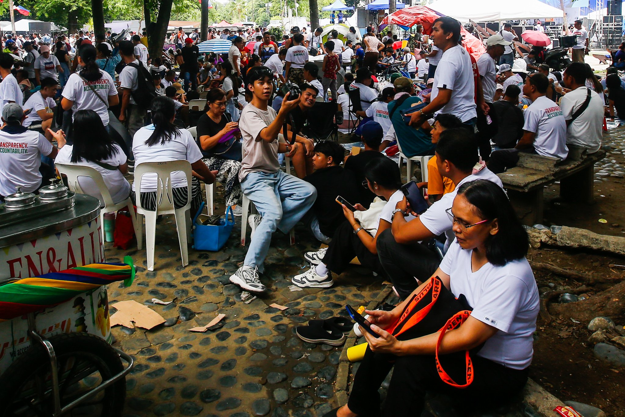 Members of Iglesia ni Cristo and their allies seek shade under trees at Liwasang Bonifacio in Manila on 02 July 2026 as they wait for the start of their protest rally. The organizers relocated the rally from the EDSA People Power Monument in Quezon City after their permit to hold the event there was revoked.