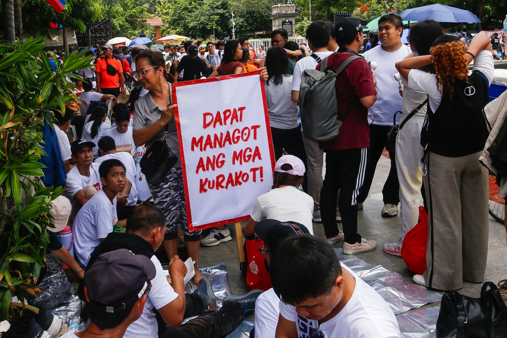 Members of Iglesia ni Cristo and their allies seek shade under trees at Liwasang Bonifacio in Manila on 02 July 2026 as they wait for the start of their protest rally. The organizers relocated the rally from the EDSA People Power Monument in Quezon City after their permit to hold the event there was revoked.