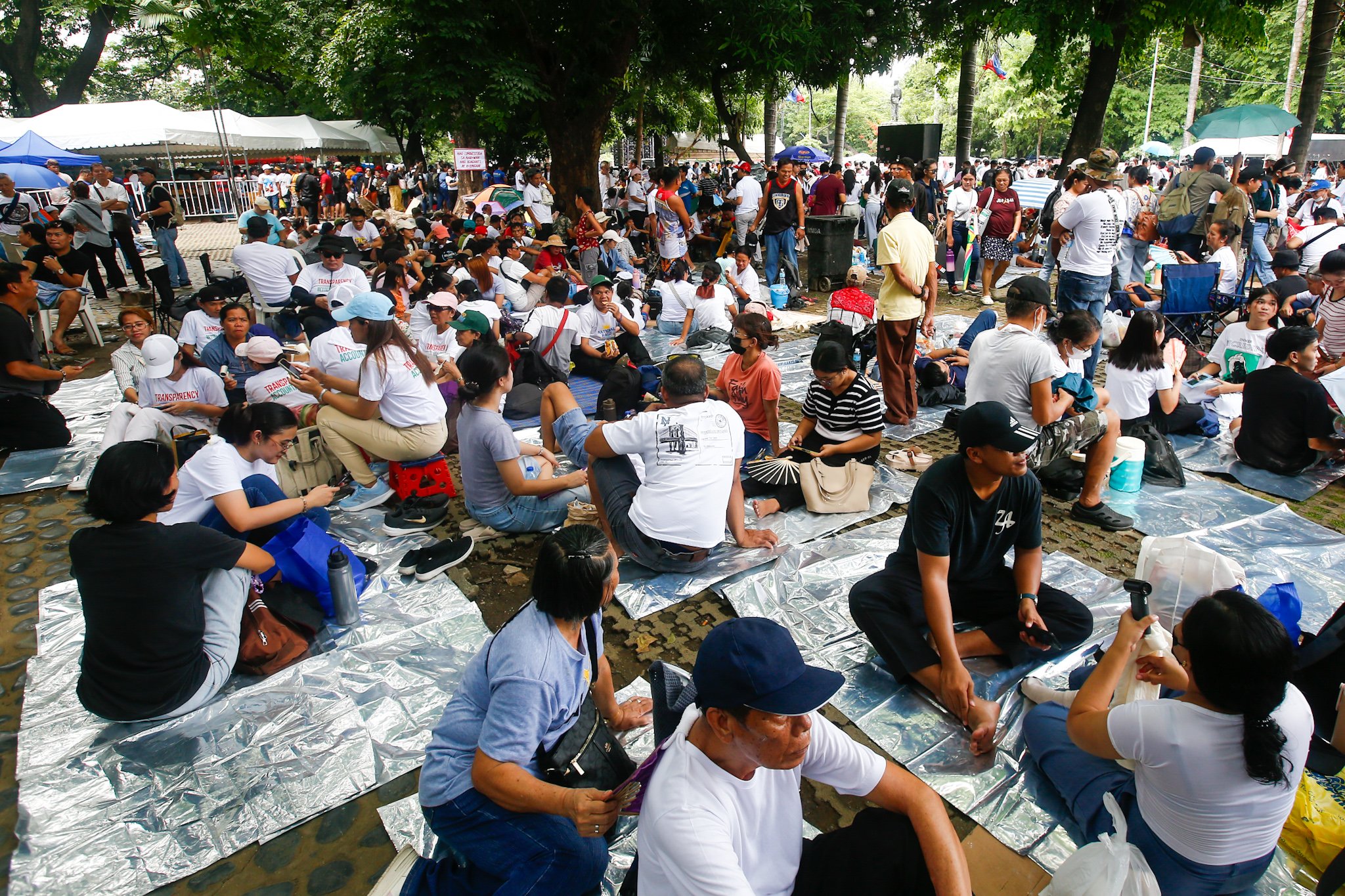Members of Iglesia ni Cristo and their allies seek shade under trees at Liwasang Bonifacio in Manila on 02 July 2026 as they wait for the start of their protest rally. The organizers relocated the rally from the EDSA People Power Monument in Quezon City after their permit to hold the event there was revoked.
