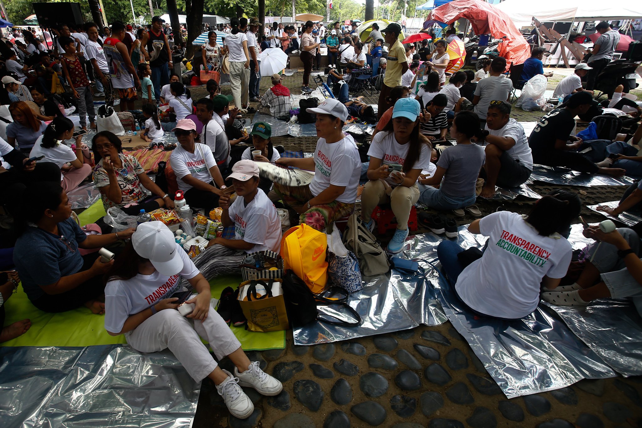 Members of Iglesia ni Cristo and their allies seek shade under trees at Liwasang Bonifacio in Manila on 02 July 2026 as they wait for the start of their protest rally. The organizers relocated the rally from the EDSA People Power Monument in Quezon City after their permit to hold the event there was revoked.