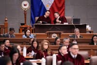 Senate President Win Gatchalian (left) and Presiding Officer Francis Escudero (right) confer during the impeachment trial of Vice President Sara Duterte, as Senate judges and staff take in the proceedings.