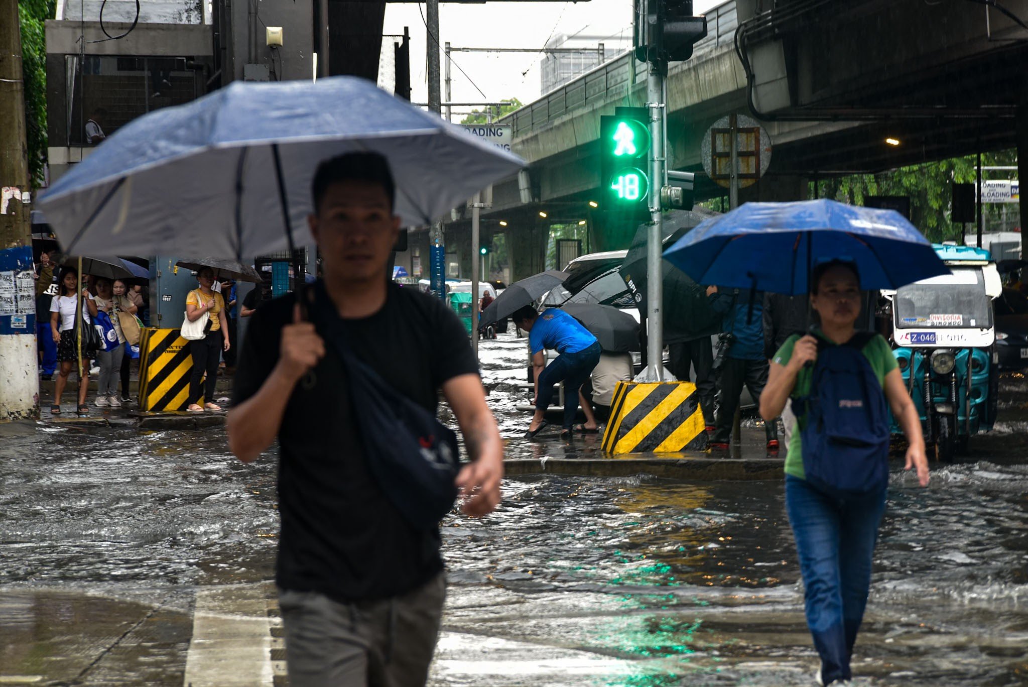 Pedestrian wade through gutter-deep flood in Manila, on July 10
