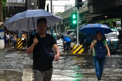 Pedestrian wade through gutter-deep flood in Manila, on July 10