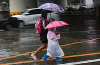 A woman and a child walk along EDSA in Quezon City under an umbrella as rain falls. PAGASA said two low-pressure areas may bring scattered rains over Metro Manila on Wednesday.