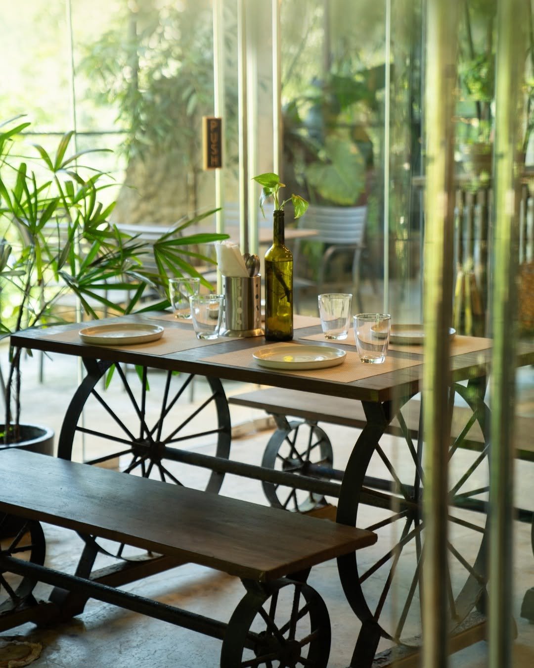 THIS industrial style dining table and bench set featuring wagon wheels is perfecty set against a lush green backdrop.