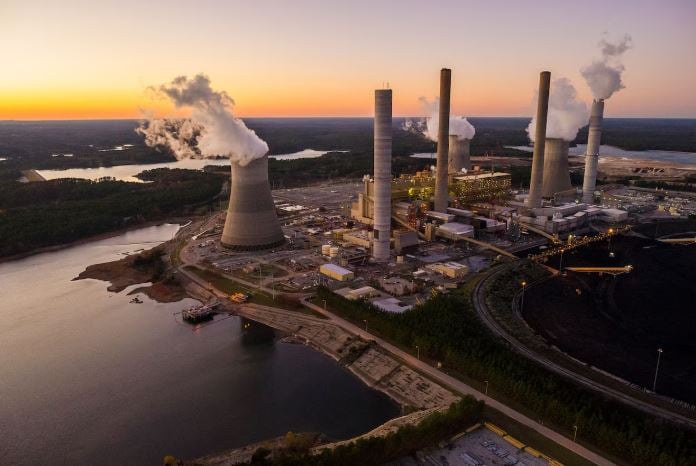 Steam and smoke rise from the cooling towers and chimneys of a power plant.